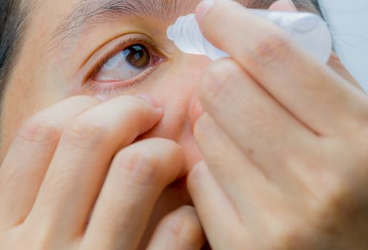 Adult Asian woman applying eye drops in her brown eyes. Eye care concept