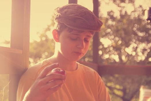 The young boy is sitting on a verandah and eatting fresh apples. Dreamy and romantic image. Summer and happy childhood concept. Added retro filter.