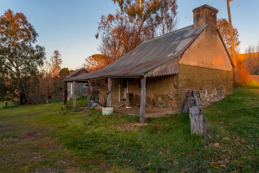 Rustic old farm house with its render exposing what looks like hand cut irregular shaped stones that formed the walls of the building with many gaps and felled tree trunks to hold up a verandah.