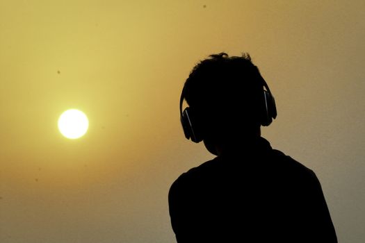 Silhouette of man with headphones on sunset sky background. Silhouette of happy man listening music.