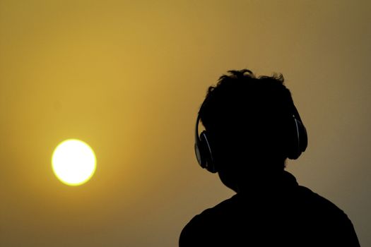 Silhouette of man with headphones on sunset sky background. Silhouette of happy man listening music.