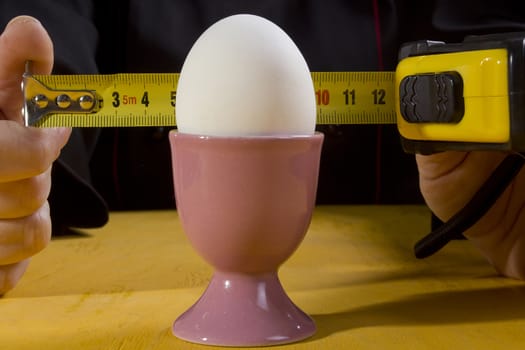 Egg in the holder and hands of the cook with a tape measure