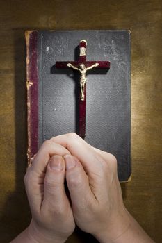 Female hands with a crucifix and an old book