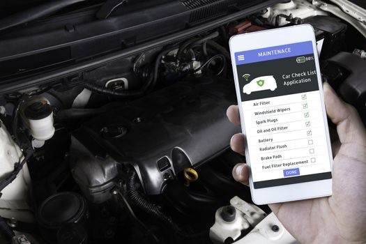 Car engine room shows all part of car and smart phone display maintenance program.