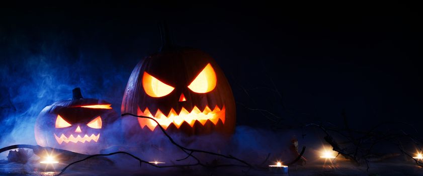Halloween pumpkins head jack o lantern and candles in blue light and mist