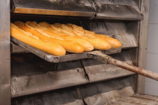 Baker taking out fresh baked bread from the industrial oven