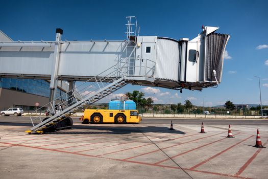 Jet bridge, boarding bridge on airport with yellow tow tractor beneath