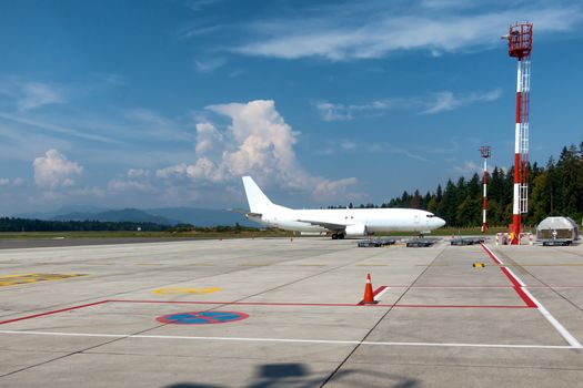 White Cargo Jet on Airport with clouds and blue sky in background, red and white airport towers and large apron, copyspace
