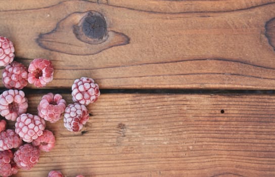 Several frozen raspberries, covered with fruit, lie on the wooden background from the top left