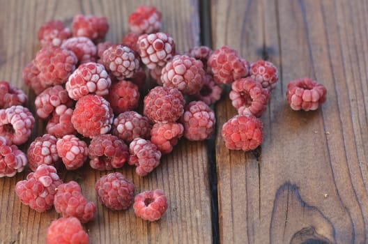 Many of the frozen berries of raspberries lie on the wooden background from the top left