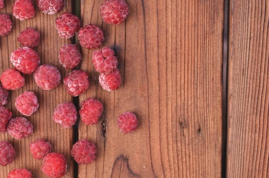 On a wooden background there are scattered raspberries