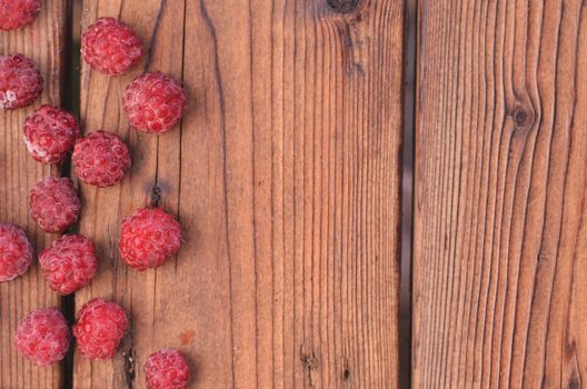 On a wooden background, raspberry is spread out on the left, a photo from above