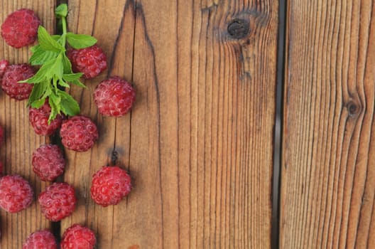 Raspberry berries are scattered on a wooden background to the left, a sprig of mint