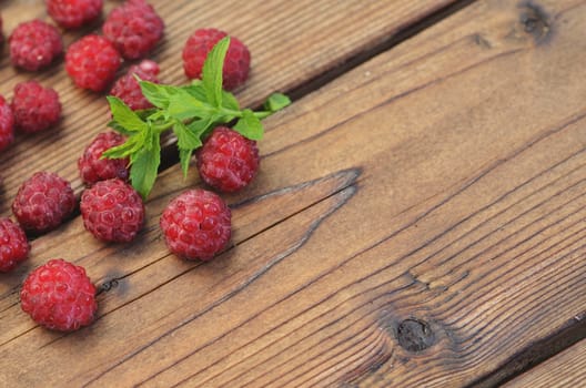 A chip of mint lies among the raspberry berries on the left on a wooden background
