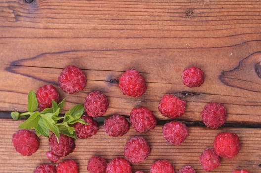 A chalk of mint lies among the raspberry berries on the bottom of the wooden background, a photo from above