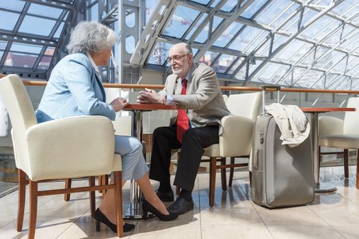 Senior couple of tourists waiting for their flight sitting with suitcase and talking