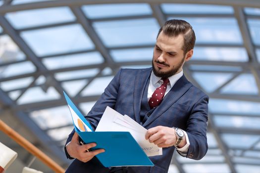 Portrait of mature businessman holding binder and documents over modern building interior background