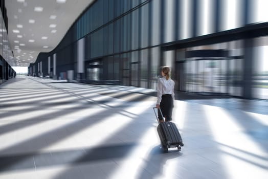 Business woman in formal clothing walking with wheeled bag at airport terminal