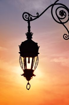 Close up side view of old vintage antique street lamp lantern over bright evening sunshine and vivid sunset sky