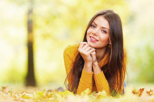 Young cute woman laying on dry leaves in autumn park