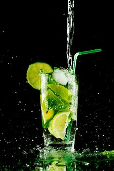 Pouring fresh mojito cocktail in glass isolated on black background