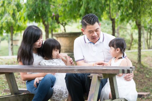 Asian family. Parents and children sitting at outdoor park. Empty space on wooden table.