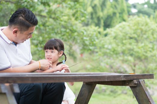 Asian family. Father and child sitting at outdoor park. Empty space on wooden table.
