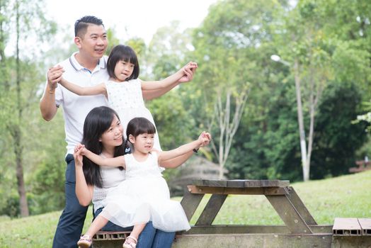 Asian family portrait. Parents and children playing at outdoor park. Empty space on wooden table.