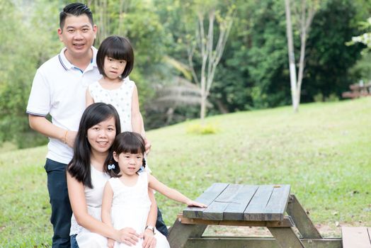 Asian family portrait. Parents and children at outdoor park. Empty space on wooden table.