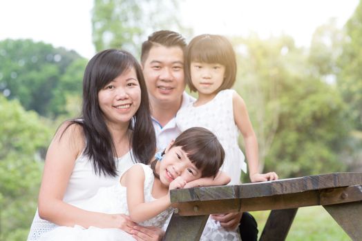 Asian family portrait. Parents and children sitting at outdoor park. Blank space on wooden table.