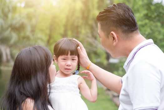Parents comfort crying daughter at outdoor park. Asian family outdoors portrait.