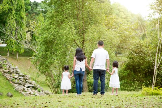 Asian family outdoors. Parents and children holding hands and walking at park. Rear view.