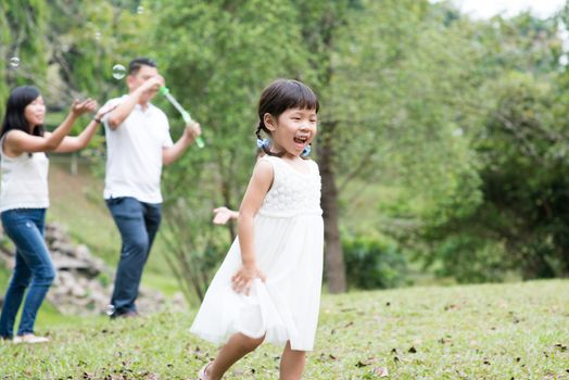 Parents and children playing soap bubbles at park. Asian family outdoors activity.