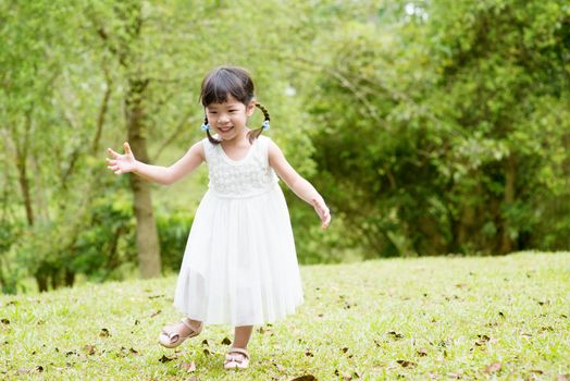 Happy little girl running at green park. Asian family outdoors portrait.