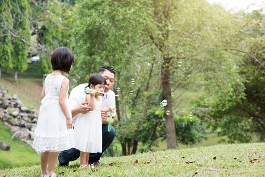 Parents and children blowing soap bubbles at garden park. Asian family outdoors activity.