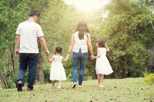 Asian family outdoors. Parents and children holding hands and walking at garden park. Rear view.