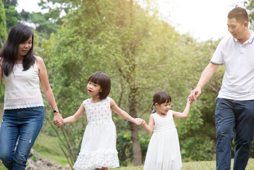 Asian family outdoors. Parents and children holding hands and walking at park. 