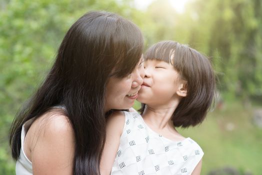 Little girl kissing mother at green park. Asian family outdoors activity.