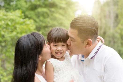 Parents kissing child at green park. Asian family outdoors activity.