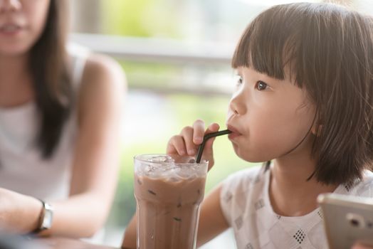 Asian child drinking iced chocolate at cafe. Natural light outdoor lifestyle.