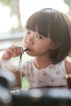 Young Asian girl drinking iced chocolate at cafe. Natural light outdoor lifestyle.