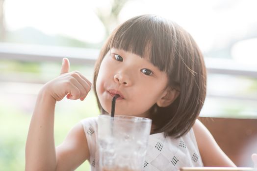 Young Asian girl drinking iced beverage at cafe. Natural light outdoor lifestyle.