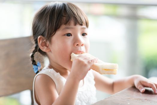 Cute Asian child eating butter toast at cafe. Outdoor family lifestyle with natural light.