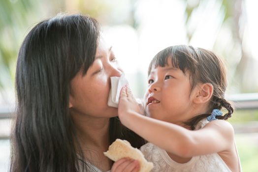 Child help mom to wiping mouth at cafe. Asian family outdoor lifestyle with natural light.
