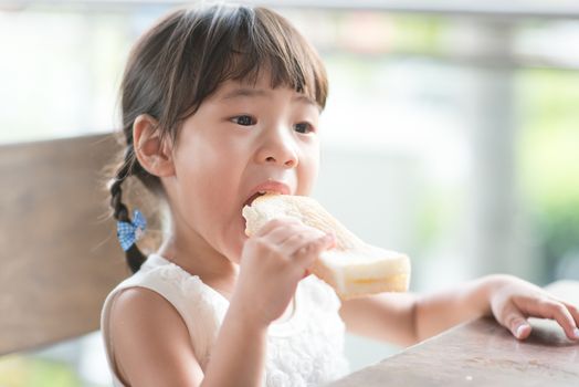 Asian child eating butter toast at cafe. Outdoor family lifestyle with natural light.