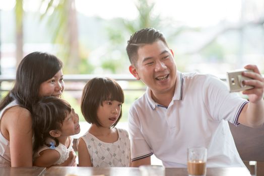 Asian family taking self photo with smart phone at cafe. Outdoor lifestyle with natural light.