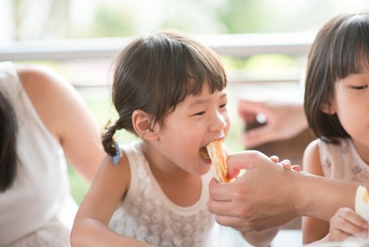 Adult feed bread to child at cafe. Asian family outdoor lifestyle with natural light.