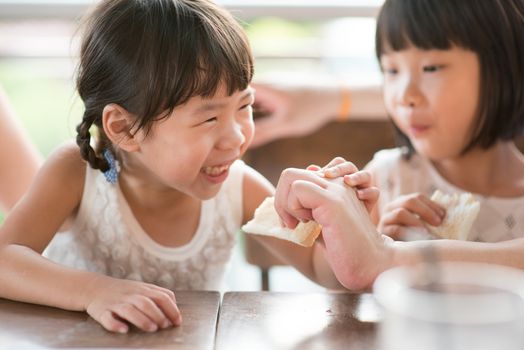 Parent feeding bread to child at cafe. Asian family outdoor lifestyle with natural light.