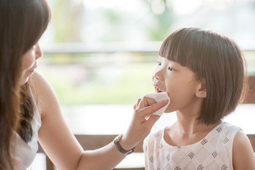 Mom wipes mouth for her child at cafe. Asian family outdoor lifestyle with natural light.