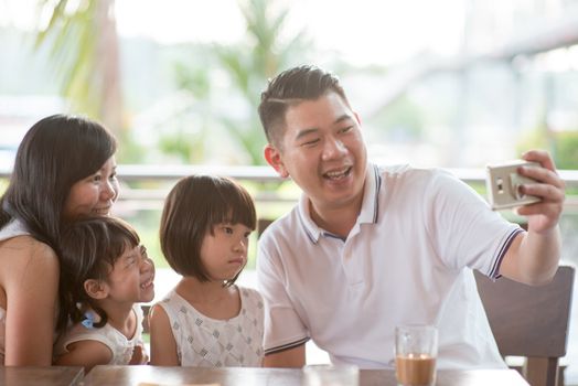 Asian family taking selfie with smart phone at cafe. Outdoor lifestyle with natural light.